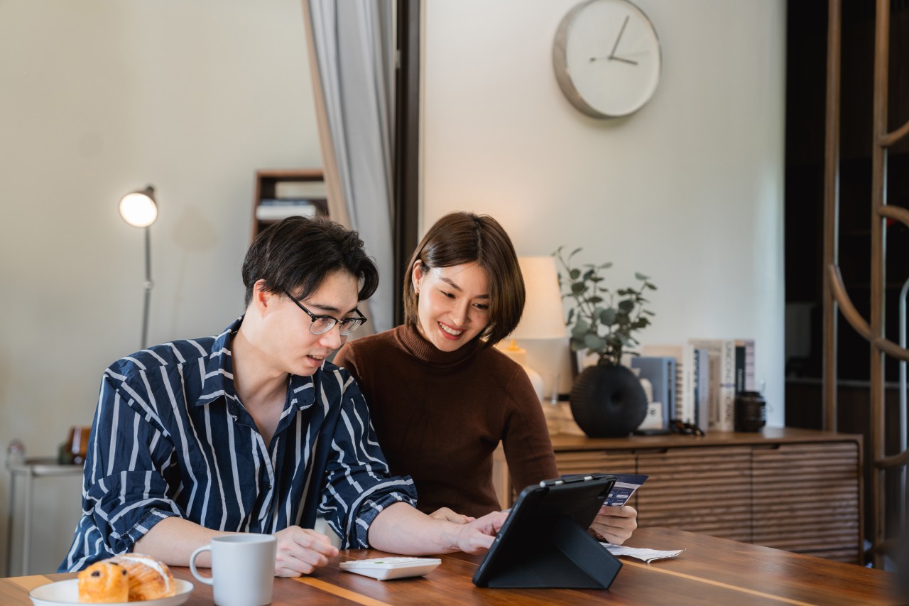Happy young Asian couple using digital tablet while going through documents together at home.